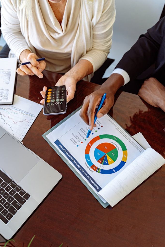 person-in-white-long-sleeve-shirt-holding-black-smartphone-5816291 Two business professionals discussing financial documents and strategies at an office desk.