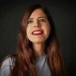 Close-up portrait of a smiling woman with long brown hair and red lipstick. Studio lighting enhances her joyful expression.